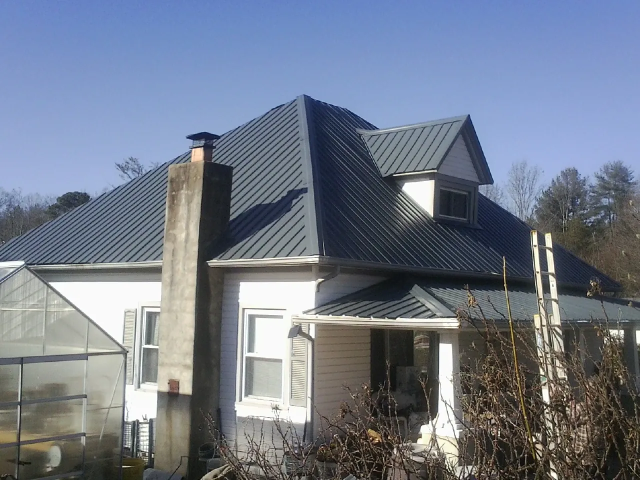 Dark blue standing seam metal roof on a white farmhouse with dormer — Slate & Tile Roof Repair by Roofing Brothers in Noxon