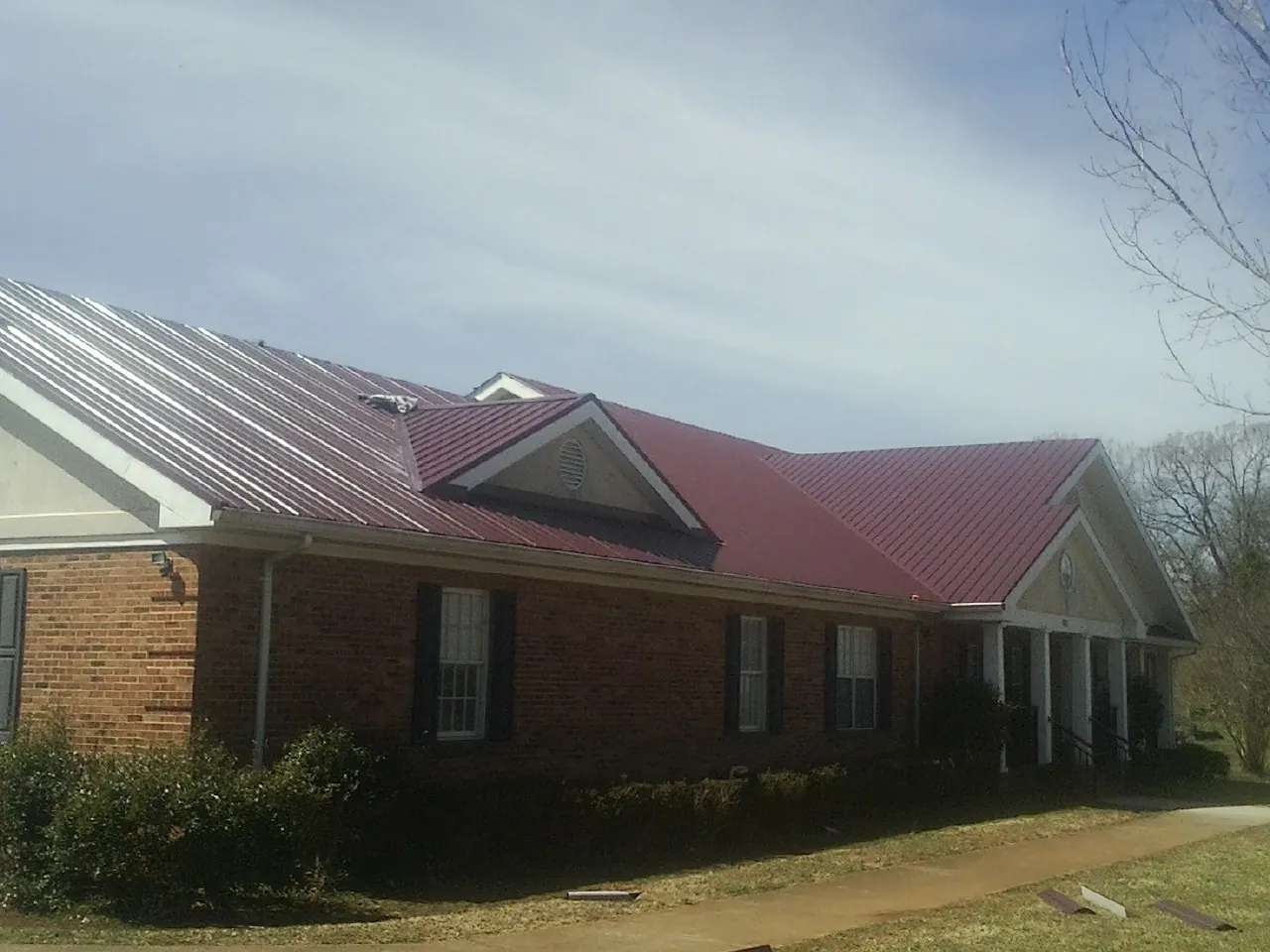 Red metal roof with gabled entries on a long brick building, from a Hail Damage Roof Repair job in Noxon