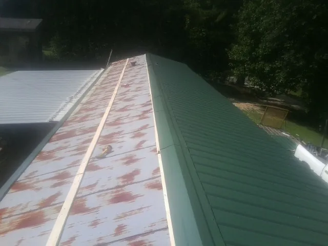 Old rusted panels beside newly installed green metal roofing — Wind Damage Roof Repair by Roofing Brothers in Noxon