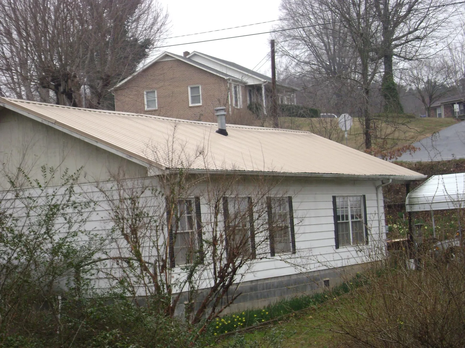 Tan metal roof on a white sided house set into a hillside — Commercial Roofing by Roofing Brothers in Noxon